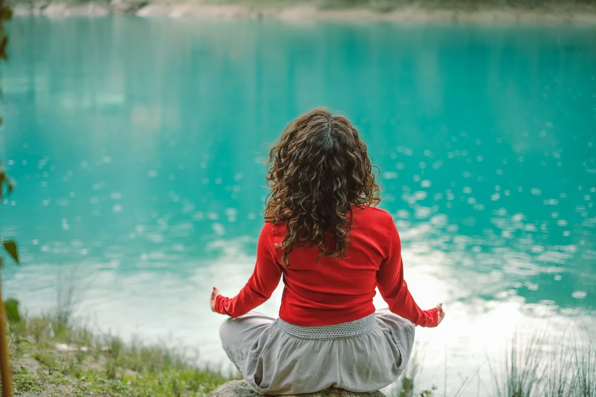 Woman meditating beside a calm lake — how to lower cortisol naturally